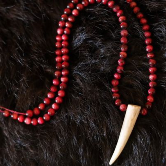 Handcrafted necklace featuring red marbled beads beautifully strung all the way to the top, with a unique deer antler pendant positioned in the center at the bottom. Displayed on a rich deep brown fur background.