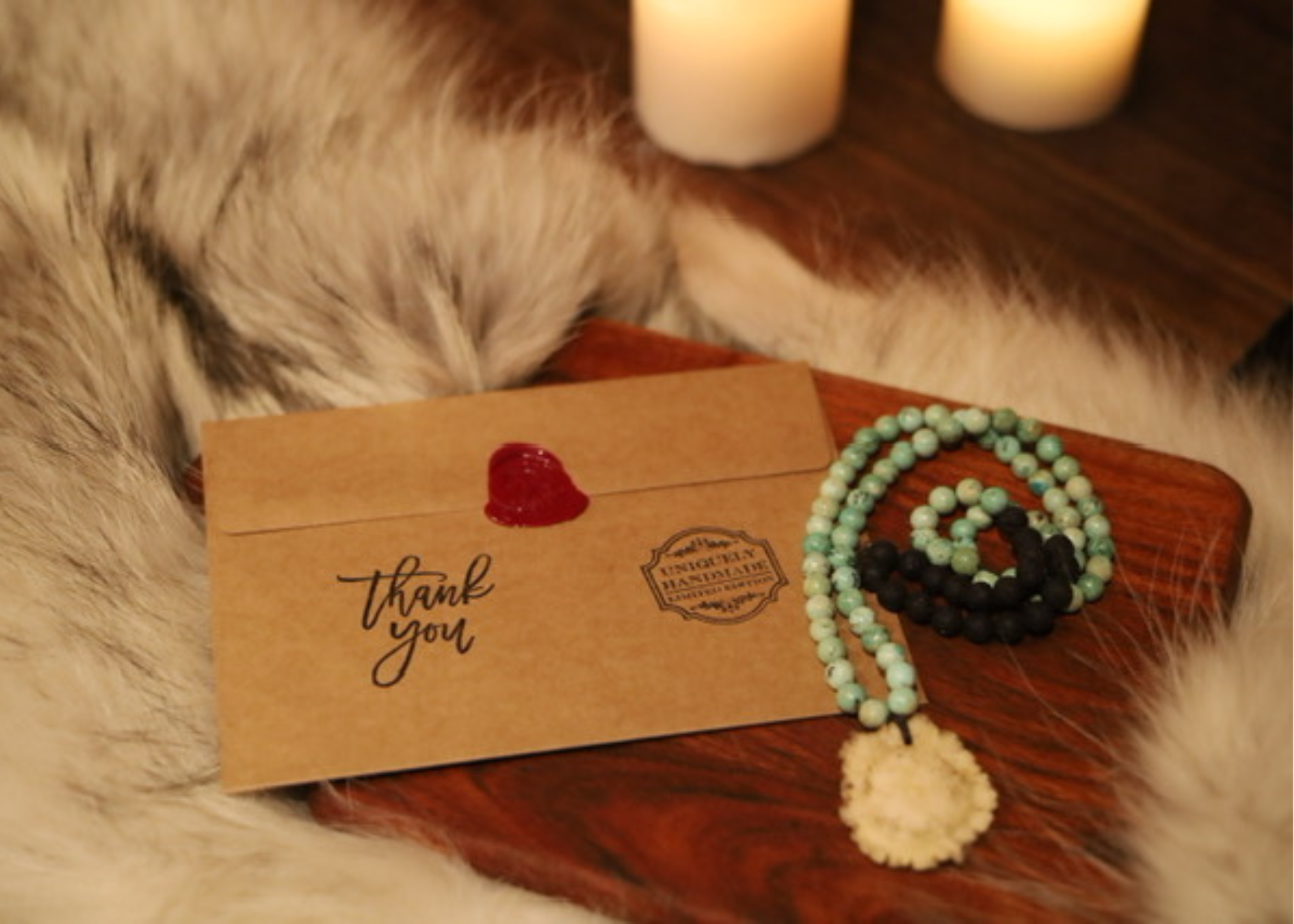 Hand-stamped and sealed envelope that says thank you on a board next to a custom necklace